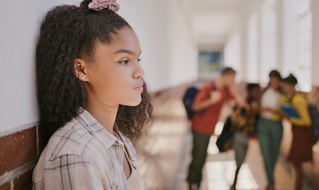 Young sad teenage girl feeling lonely and excluded at school. Female outside classroom and thinking about teen problems, bullying or trouble feeling depressed and anxiety.