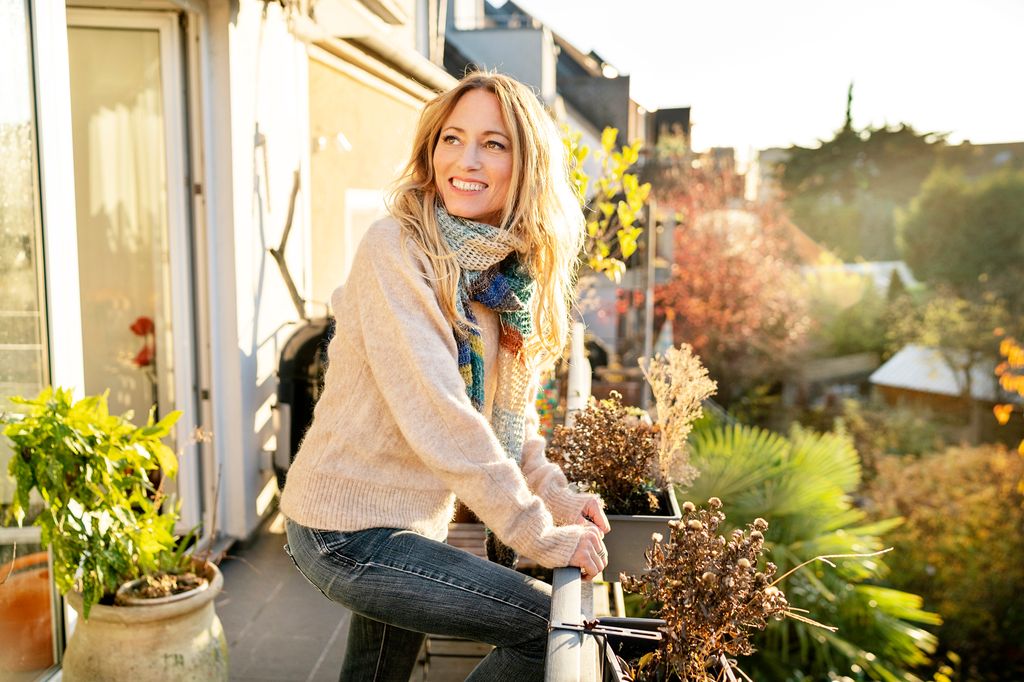 mujer sonriente mirando por su balcón en una mañana de otoño