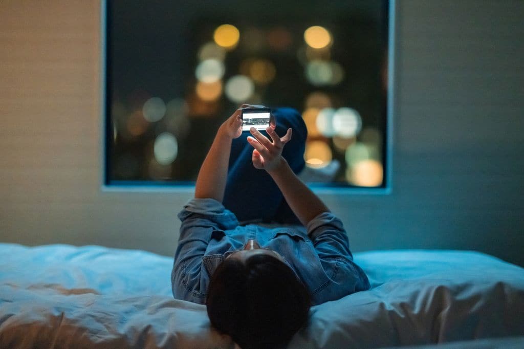 mujer mirando el móvil por la noche, mientras está en la cama