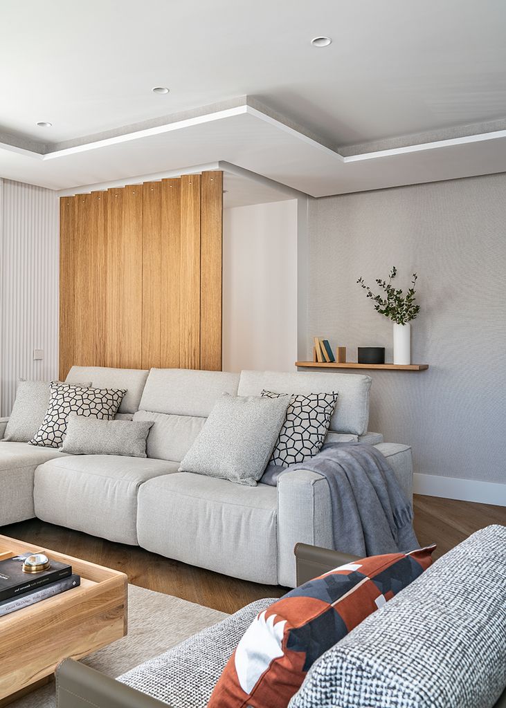 Salón con sofá gris y panel de madera. 