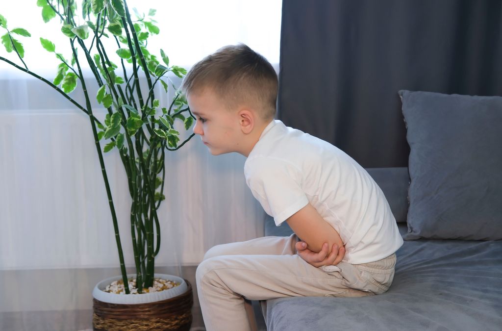Niño con gastroenteritis tocándose la tripa en el sofá por dolor