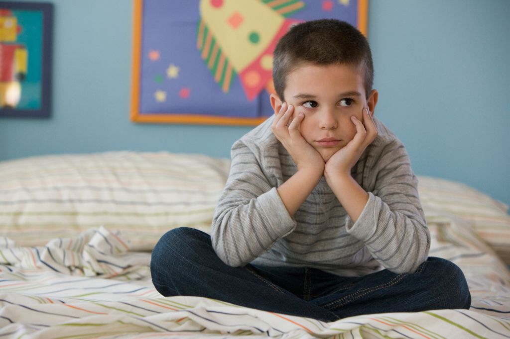 niño serio sentado en la cama