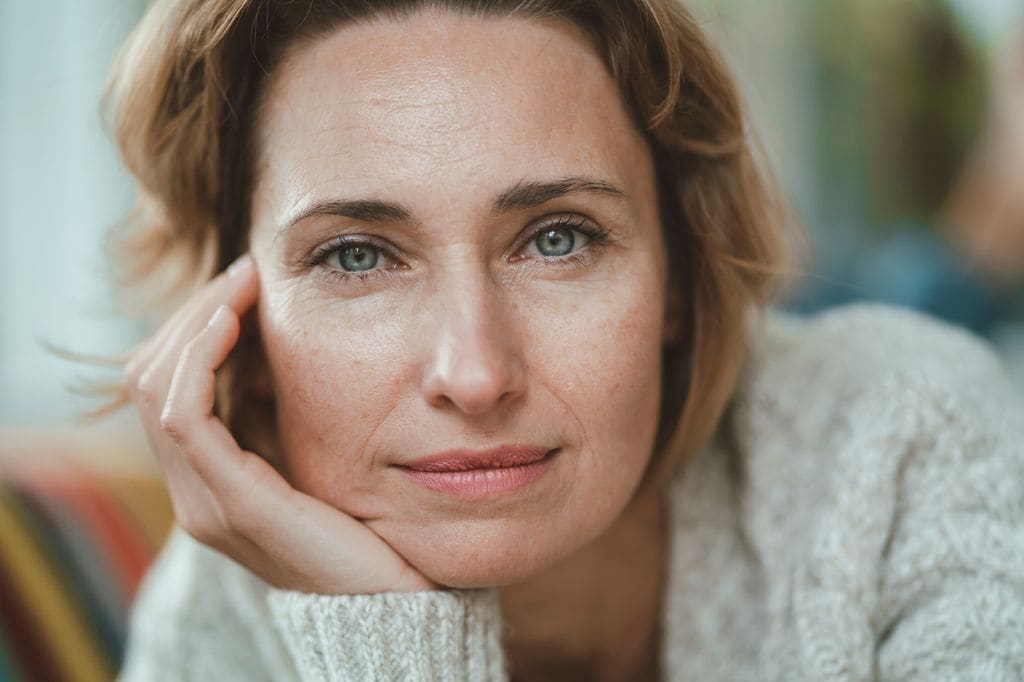 Mujer madura sonriente con la cabeza apoyada en su mano