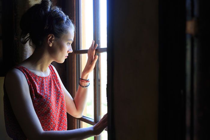 Mujer asomada a la ventana con la mano sobre el cristal