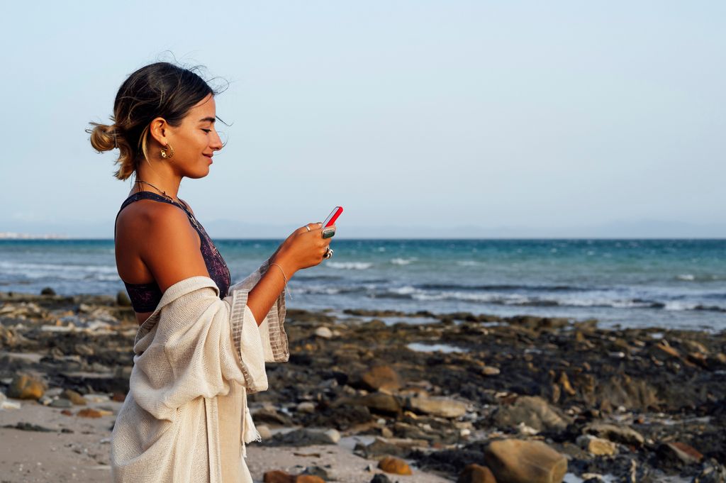 mujer sonriente usando el móvil en la playa