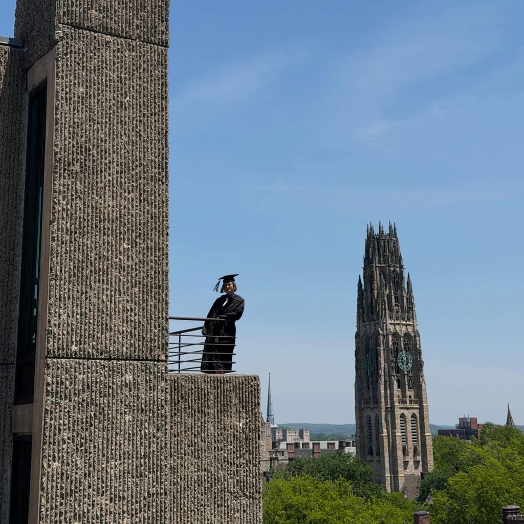 Paola con toga y birrete con la simbólica Harkness Tower de Yale de fondo