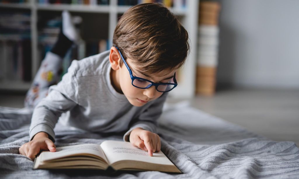 one caucasian boy lying on the floor at home in day reading a book front view copy space real people education concept