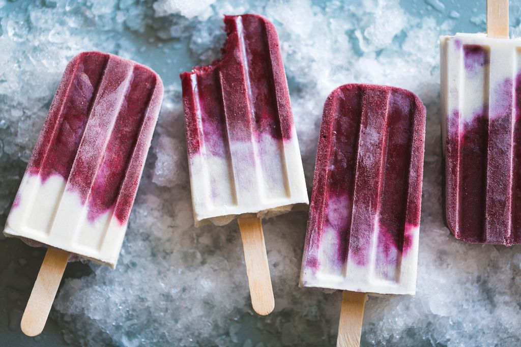 Helados en formato polo de frutas del bosque y yogur, sobre una superficie helada.