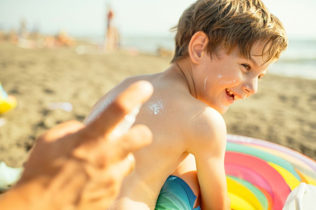 Niño pequeño en la playa mientras le aplican crema protectora