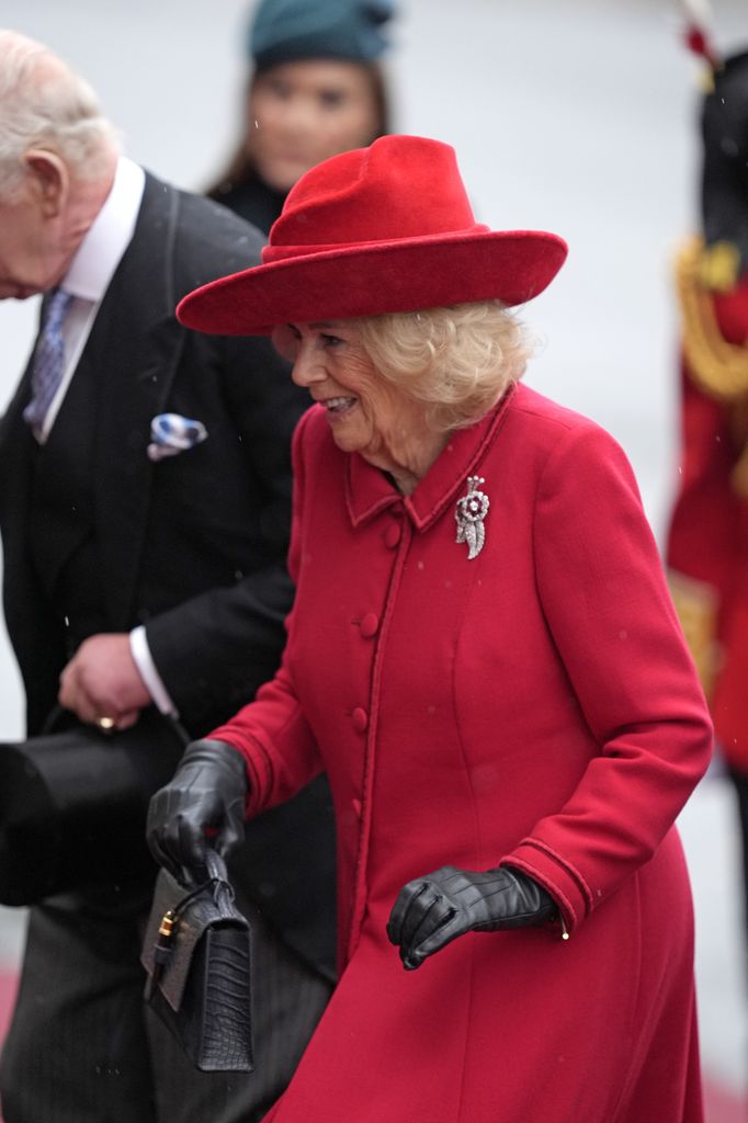 La reina Camilla, de rojo con el broche de diamantes y rubíes de la Reina Madre