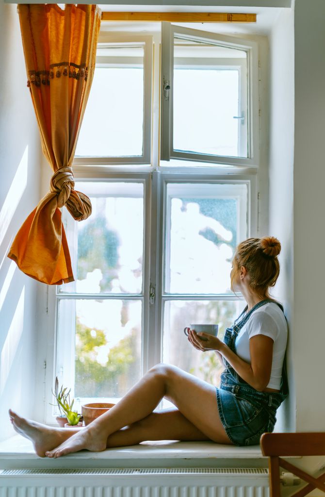 Mujer joven con una taza de té mirando por la ventana