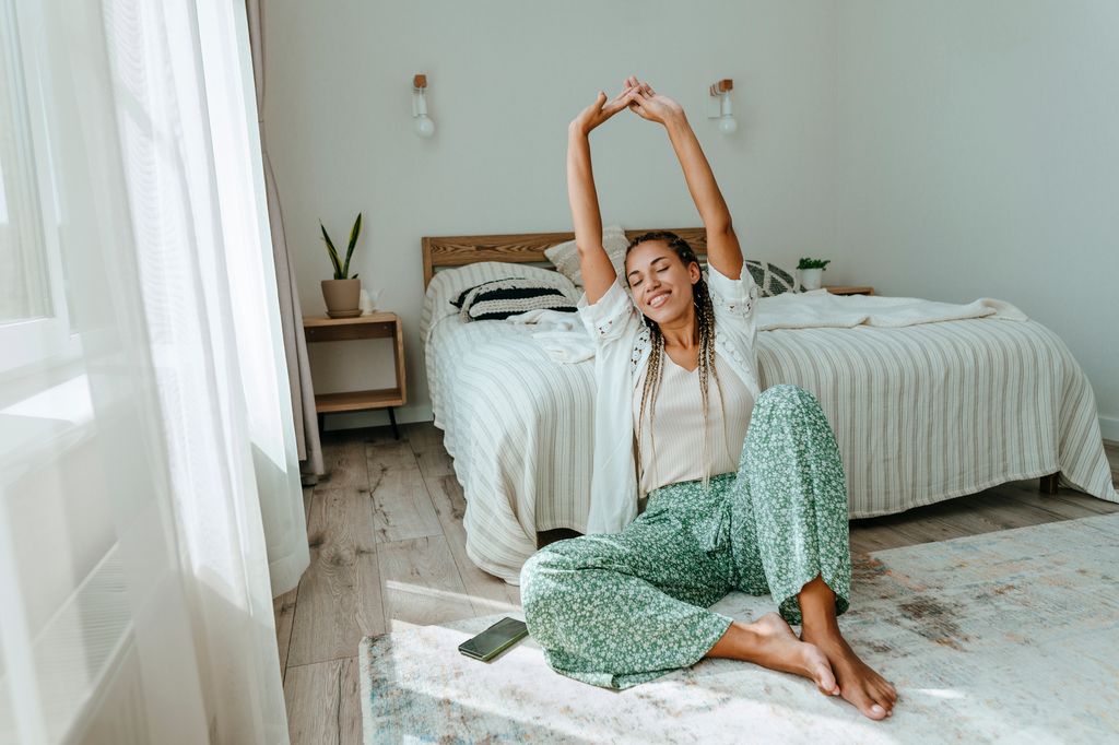 Mujer delante de la cama estirando y feliz