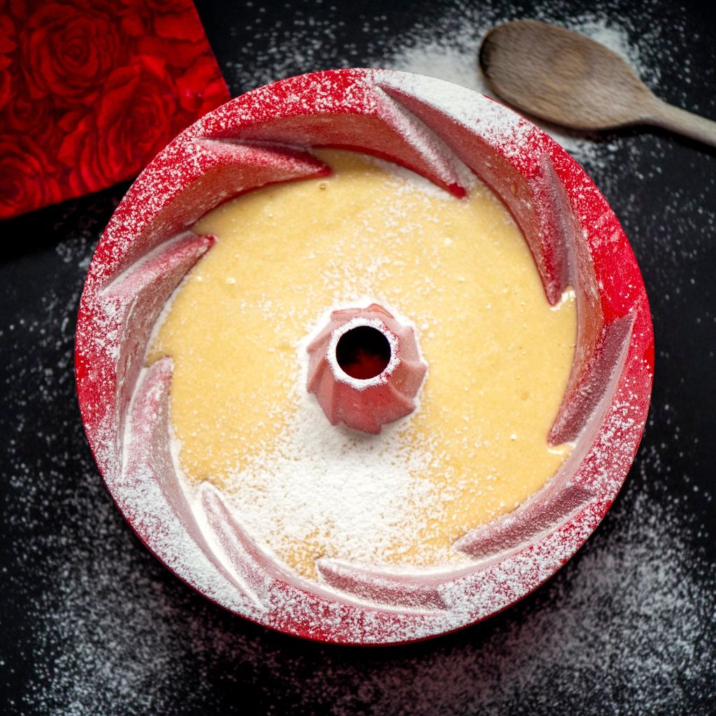 Lemon Cake pan with Raw Cake dough on wooden table and a red silicone pan.