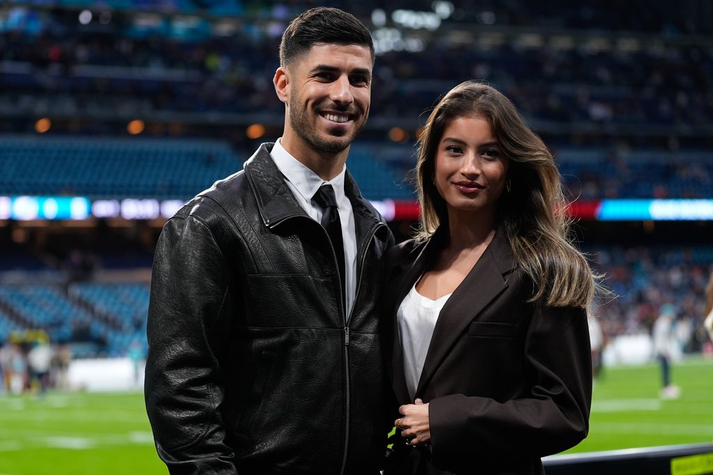 Marco Asensio y una mujer sonrientes en un estadio de fútbol.