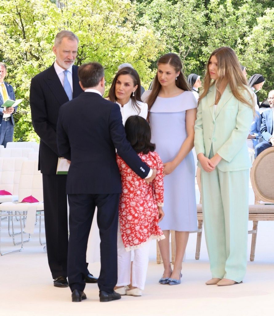 Felipe VI, Letizia y sus hijas con una niña en ceremonia al aire libre.