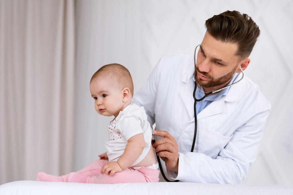 Pediatra auscultando a un bebé con enfermedad respiratoria