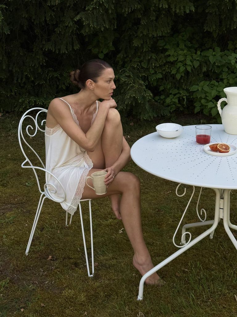 Modelo morena con camisón de Eberjey junto a una mesa blanca en un jardín