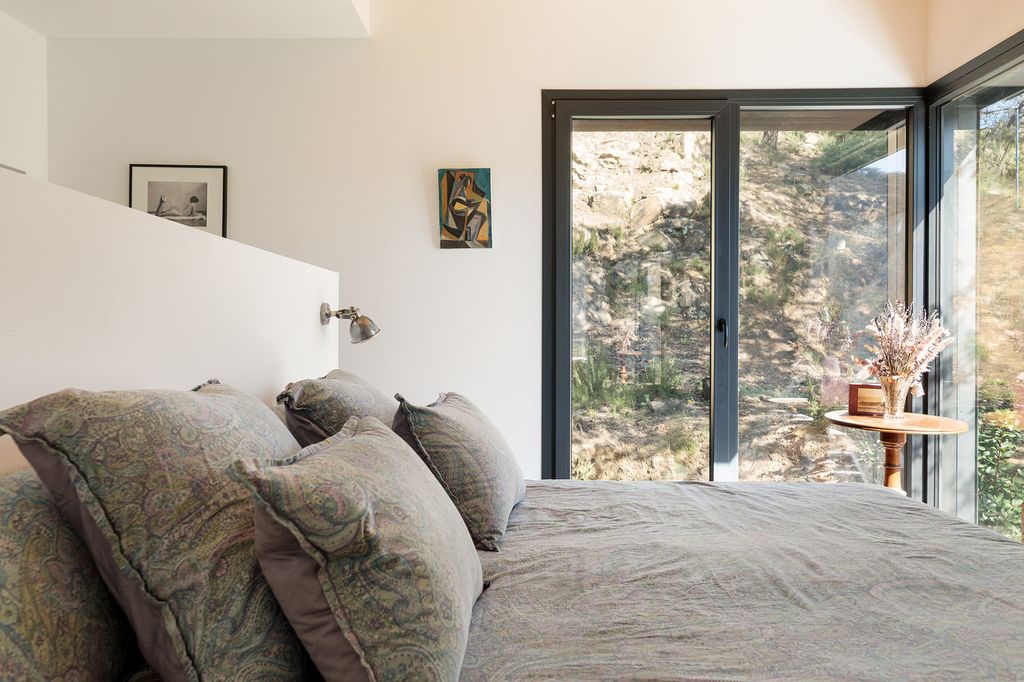 Dormitorio con cabecero de obra, salida a terraza, ropa de cama gris, apliques en el cantero, mesa auxiliar de madera y cuadros