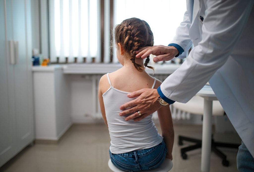 Niña en consulta del médico examinando su columna vertebral