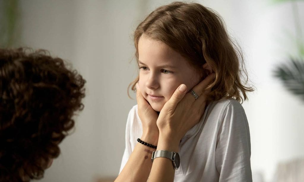 ni o triste mirando a su madre que le sostiene la cara con sus manos