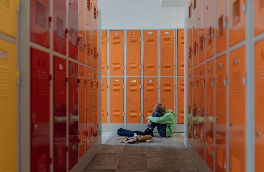Niño víctima de acoso escolar sentado en el suelo del insituto
