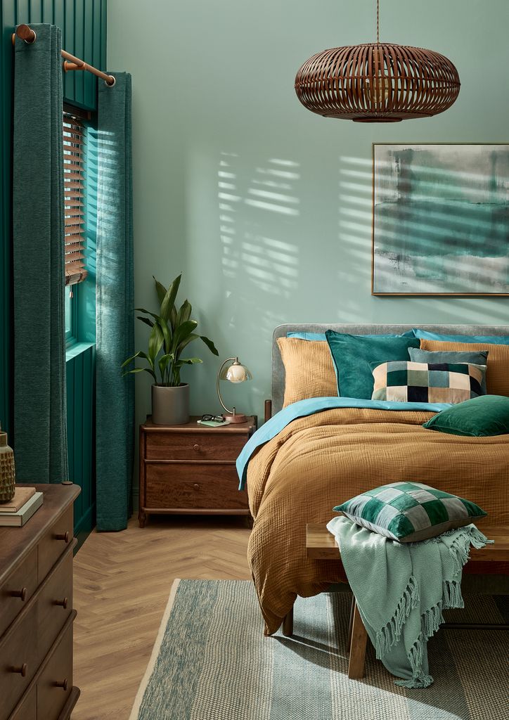 Dormitorio con paredes en verde azulado, ropa de cama marrón claro, lámpara de techo de fibras vegetales, banqueta a los pies de la cama, cuadro en la pared del cabecero 