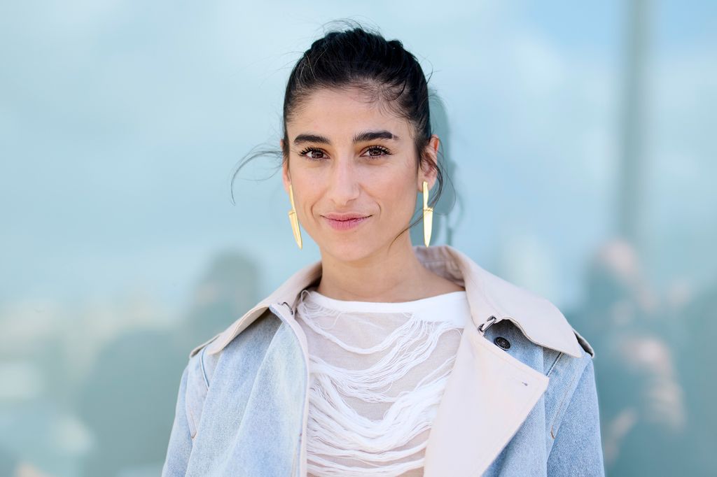 Mujer con cabello oscuro, aretes dorados y chaqueta azul posando para una foto.