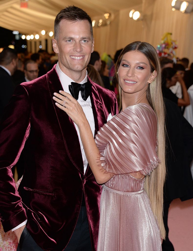 Tom Brady y Gisele Bündchen posan juntos en una alfombra roja, ambos sonrientes.