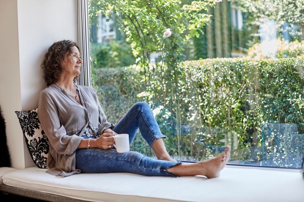 mujer madura pensativa mirando por la ventana con un café