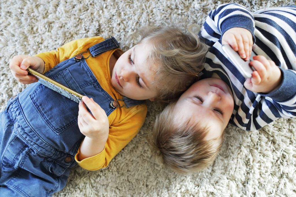 Niños pequeños tumbados viendo el móvil
