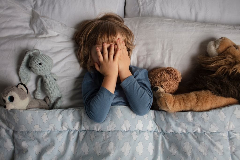 Niño con miedo en la cama rodeado de peluches