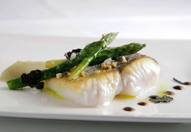 Plato de pescado con espárragos y guarnición en plato blanco.