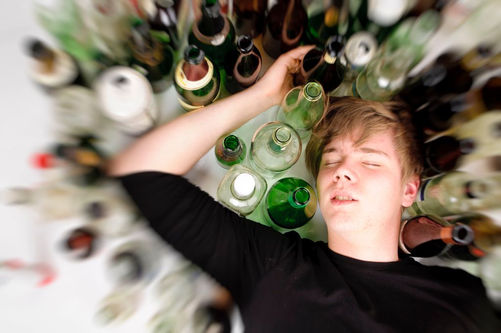 Adolescente tumbado con botellas de alcohol