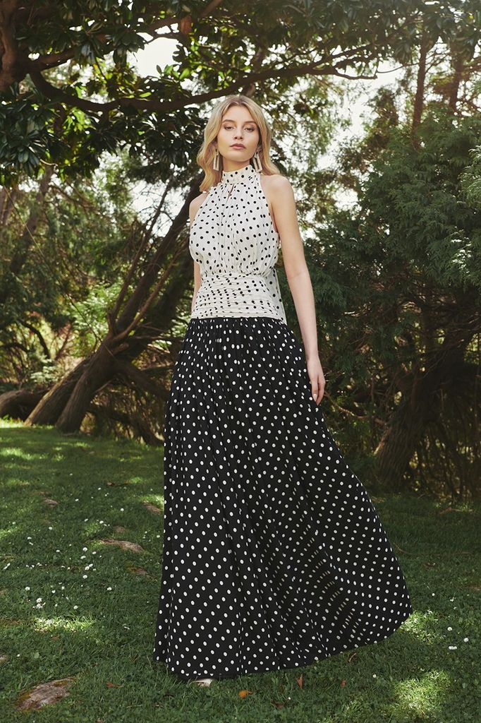 Vestido largo confeccionado en crepe fino de lunares negro y blanco, combinando con un crepe en contraste jugando con los lunares al contrario.  Cuerpo con escote halter y lazada que anuda al cuello. Escote de lágrima profundo, la abertura le da un toque muy sensual. 