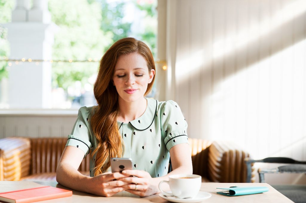 mujer sentada mirando su teléfono móvil con un café en la mesa