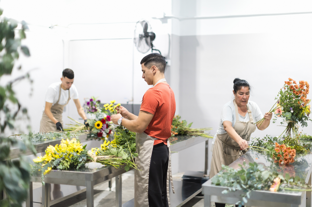 Tres trabajadores de Flores Solidarias creando arreglos florales en el taller.