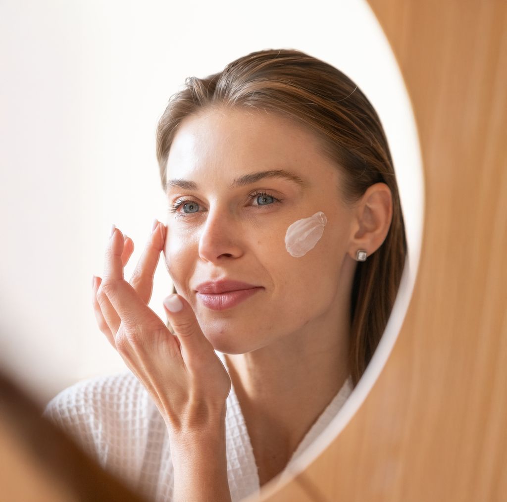 Rostro de mujer aplicándose crema en la cara mientras se mira al espejo