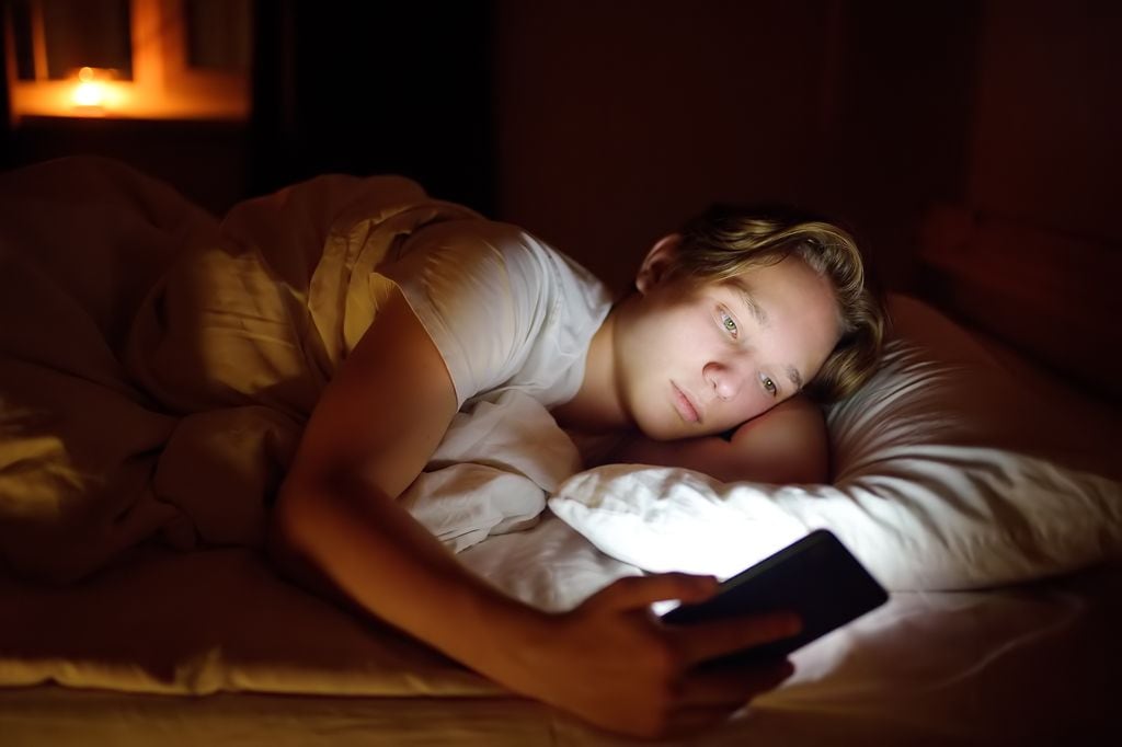 Adolescente mirando el móvil en la cama