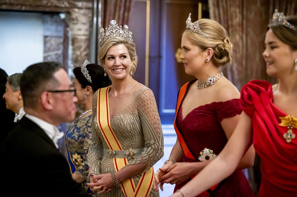 Queen Máxima de los Países Bajos, con tiara y vestido dorado, conversa con otras mujeres en un evento formal.