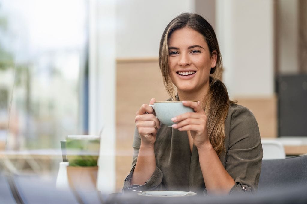 Mujer sonriendo en una terraza con una taza de té o café en una terraza
