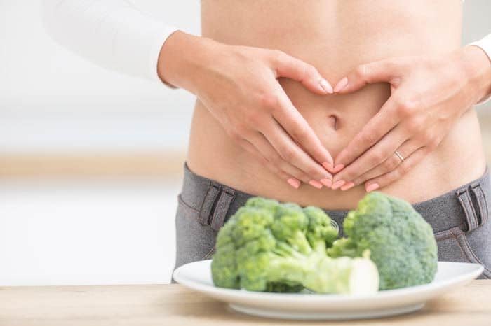 mujer con hinchazón abdominal y un plato de brócoli