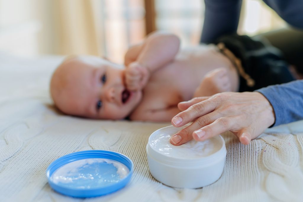 Madre cogiendo crema de un tarro para aplicar a su bebé