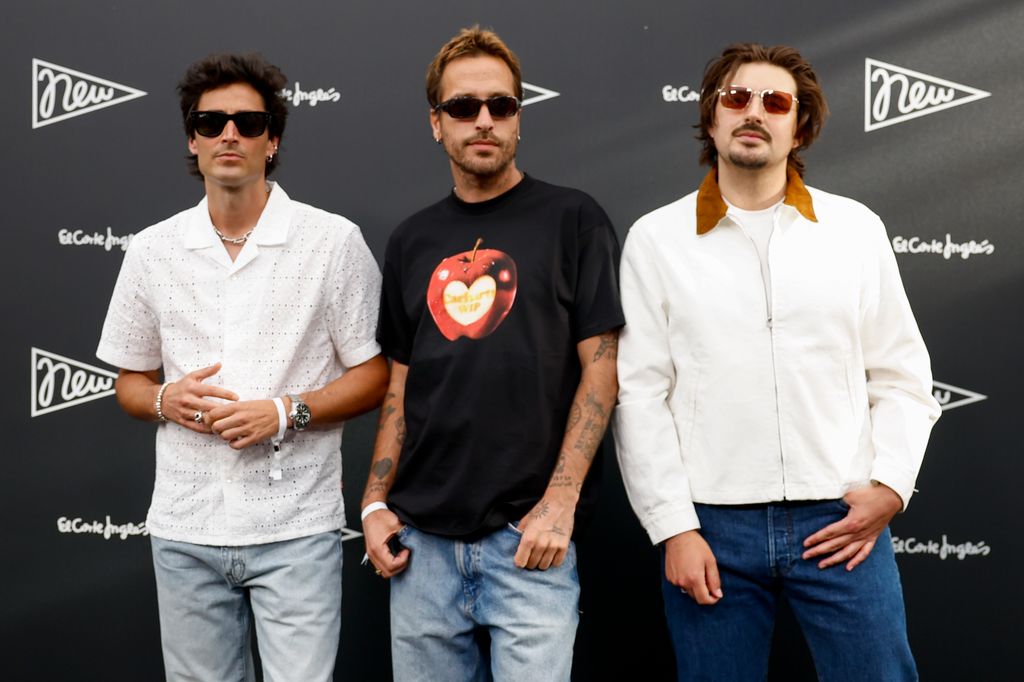 Tres hombres con gafas de sol posan juntos ante un fondo con marcas.