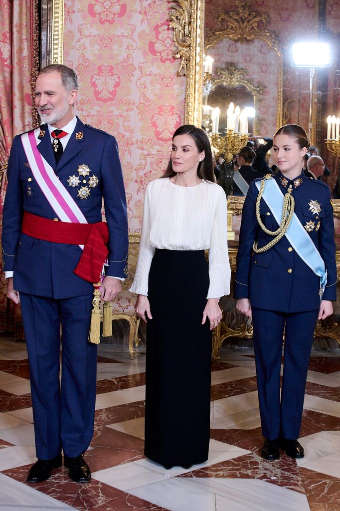 Debajo de la capa, la reina Letizia lució una falda recta y una blusa fluida blanca. 