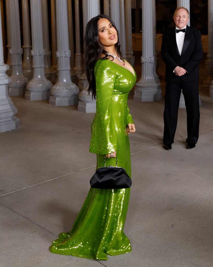 Salma Hayek posando para los fotógrafos, mientras su esposo la espera pacientemente, como todo un caballero.