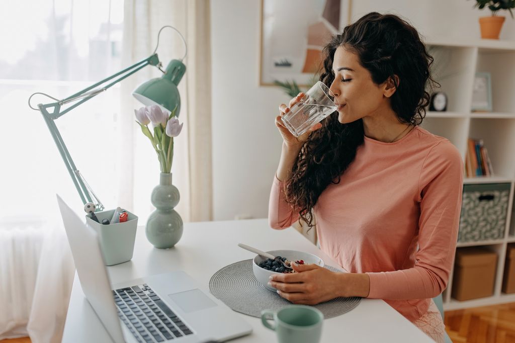 mujer bebiendo agua mientras come, en su escritorio