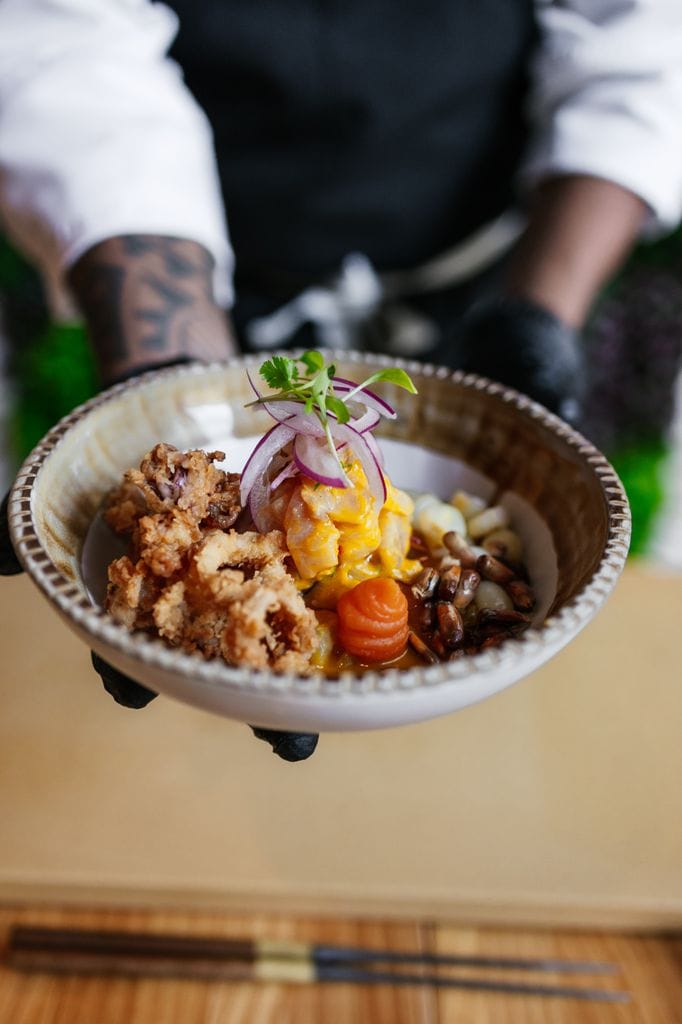 Clásico ceviche peruano de corvina salvaje, cebolla roja, bañado con leche de tigre, acompañado con choclito, boniato y cancha chulpi, coronado con cilantro de Lima Nikkei.