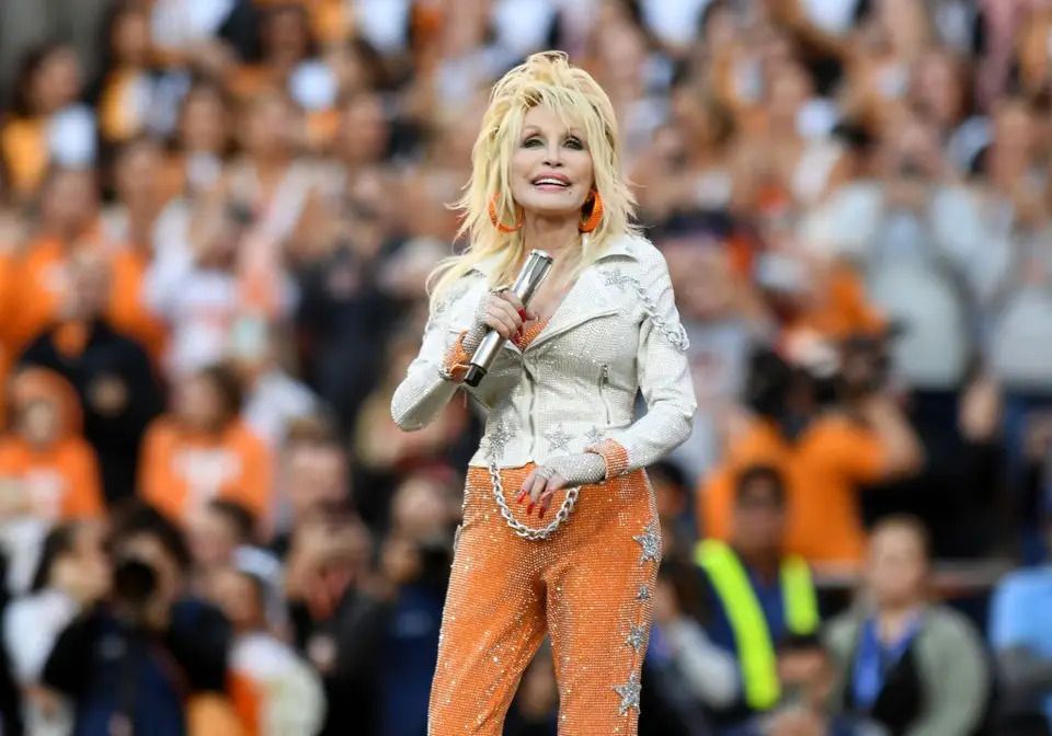 Dolly Parton aparece en el campo del Neyland Stadium vistiendo los colores naranja y blanco de los Tennessee Volunteers durante un partido de fútbol americano universitario en 2023.