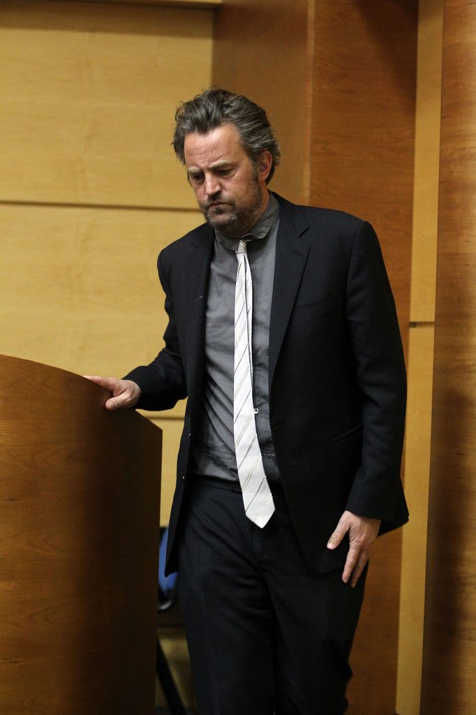 Plano medio de Matthew Perry con traje en una conferencia