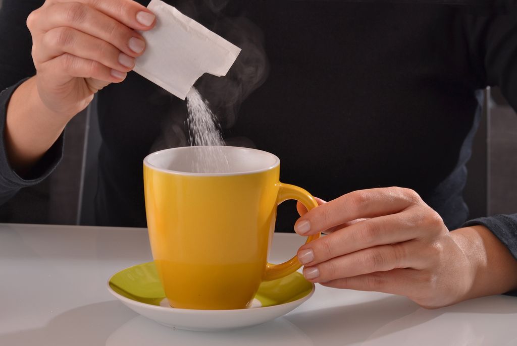 Una persona vaciando un sobre de azúcar en el café 